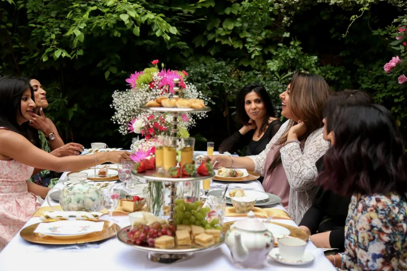 A garden afternoon tea — women in conversation around a tiered table of flowers and food